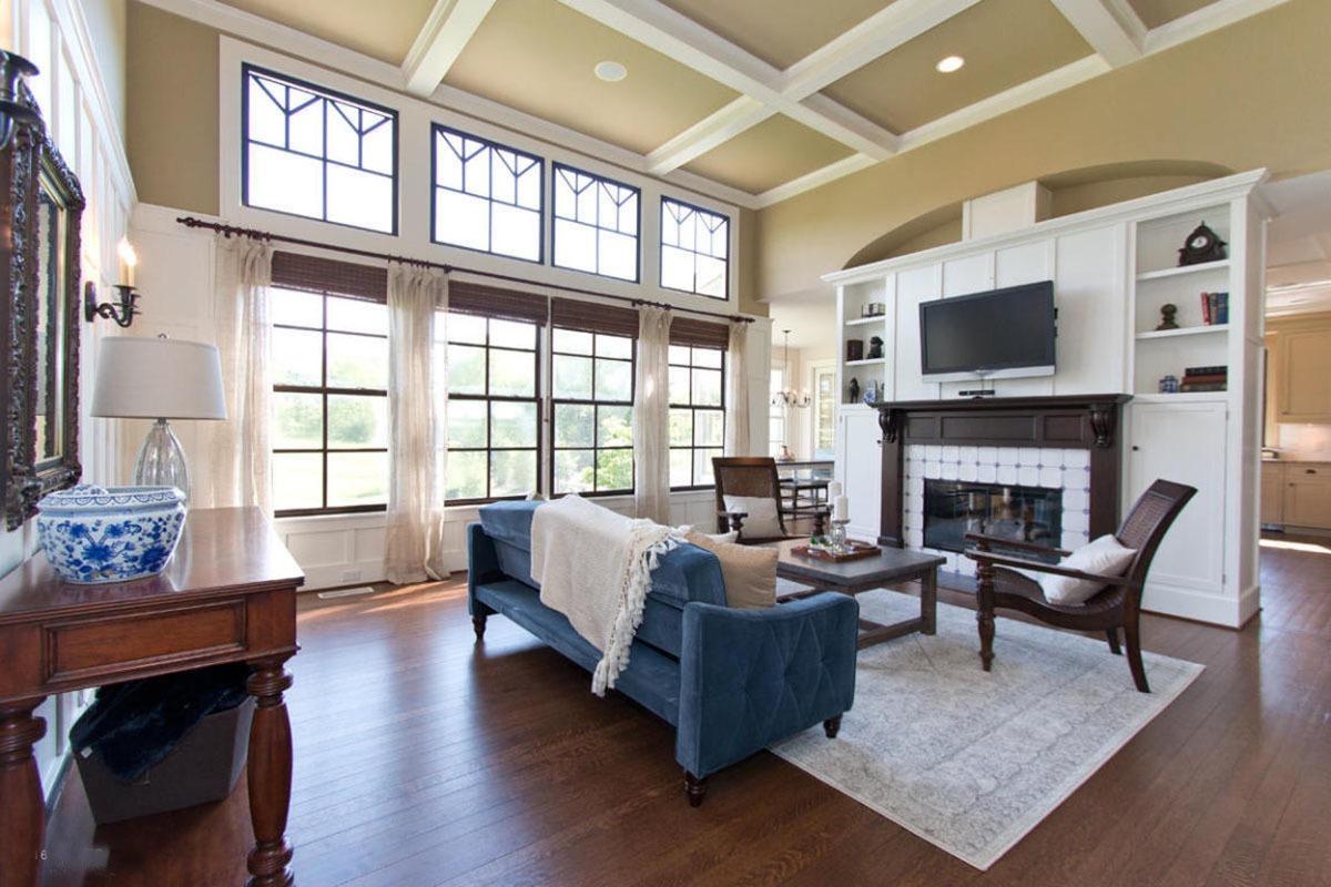 通风的客厅与方格天花板和木头框玻璃窗覆盖着柳条罗马帘和白色的窗帘。它包括一个蓝色的沙发搭配木质咖啡桌和扶手椅。