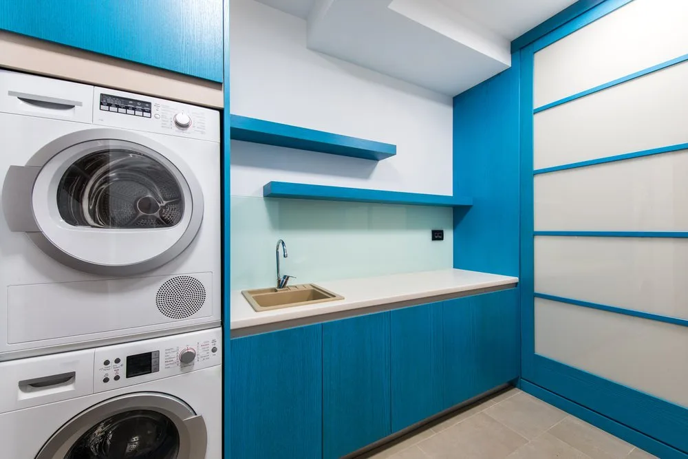 洗衣房特性堆洗衣机和干衣机用蓝色组合橱柜水槽和效用。