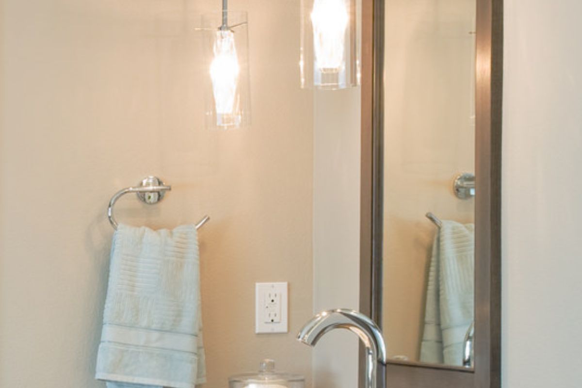 一对吊灯照亮了浴室，展示了带有铬固定装置和毛巾架的容器水槽梳妆台，以及安装在米黄色墙壁上的木框镜子。