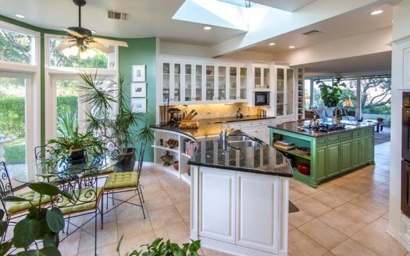 这个厨房的绿色墙壁和室内到处都是植物，看起来很清爽。中央岛和半岛的黑色柜台看起来都很时尚。