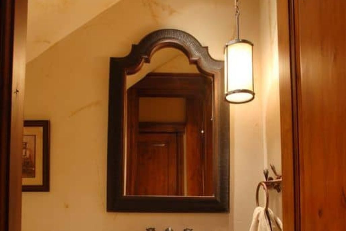 一扇木门通往这间农舍的浴室，浴室里有水槽和一面安装在拱形墙下的木制镜框镜子。