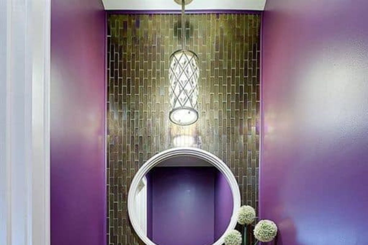 折衷的化妆室，白色的浮动容器水槽梳妆台固定在紫色的墙壁上。它配有一面圆镜子，并由一个华丽的吊坠照明。