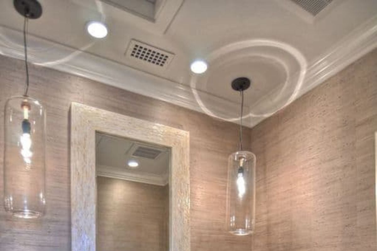 这间浴室有一个破旧的水槽梳妆台，由白色天花板上挂着的圆柱形玻璃挂件照亮。