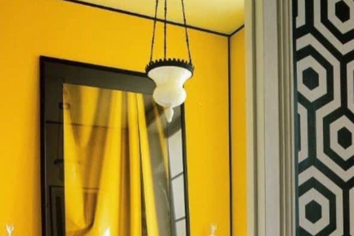 黄色浴室，配有黑色爪形浴缸和黑色镜框镜子，由独特的吊灯照亮。它包括一个坐在硬木地板上的带点的凳子。