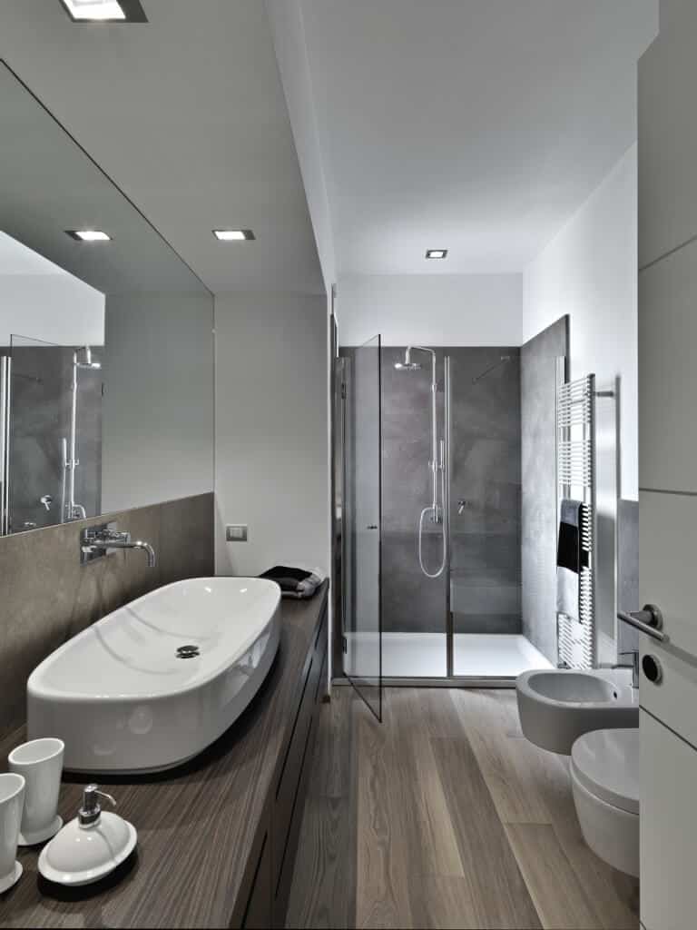 这个浴室的灰灰色色调绝对令人惊叹。白色陶瓷通过淋浴间的灰色瓷砖和华丽的硬木瓷砖和台面被赋予了生命。这是一个真正的光滑和当代的设计在其最好的。