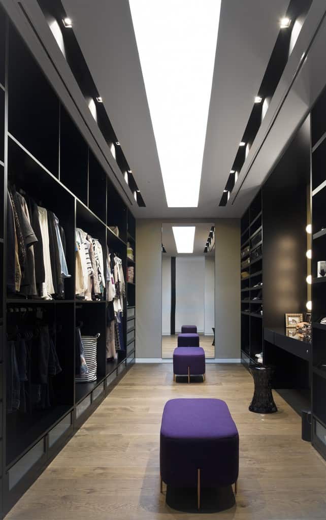 时尚的卧室衣柜，设有时尚的黑色成品橱柜和硬木地板上的紫色软脚凳。