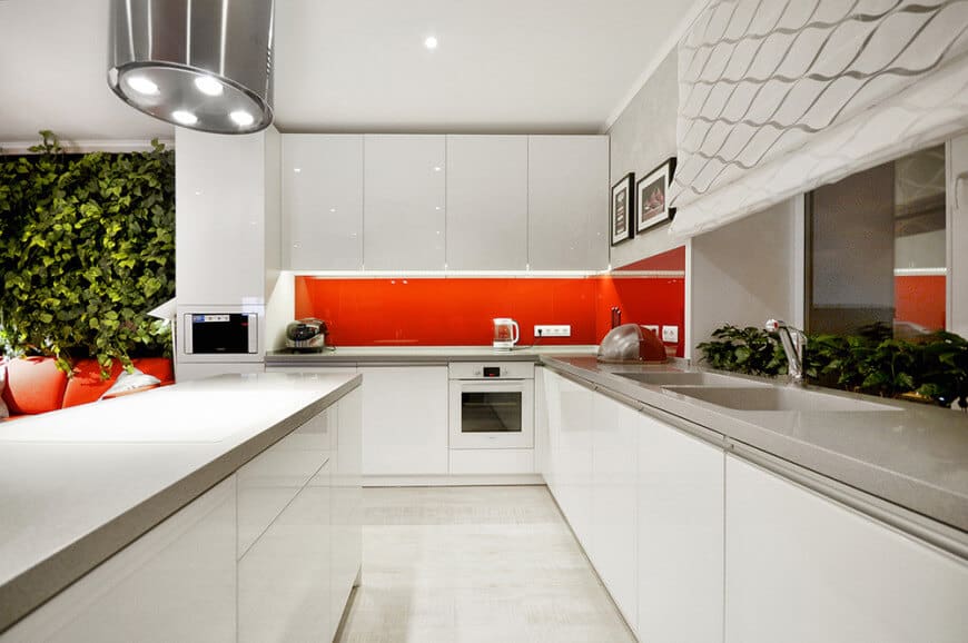 厨房布局的现代厨房。它充满了光滑的橱柜和白色烤箱，并带有充满活力的红色高光后挡板。