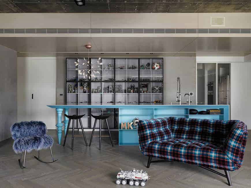 单墙厨房设有大架子和一个蓝色的中心岛，内置架子和一个早餐吧设置在时尚的灰色地板上。