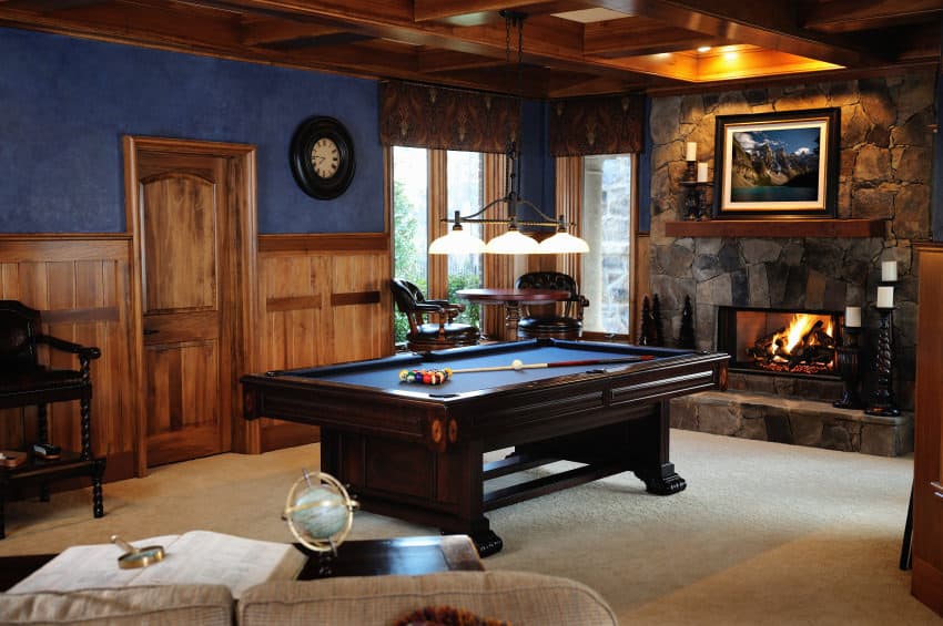 小木屋乡村风格的男子洞穴，小石面壁炉，台球桌，酒吧风格的小木桌和凳子加上沙发和茶几。这个房间里有壁炉和浅米色的地毯，散发出温暖的气息。最重要的是那张深蓝色表面的黑木台球桌。