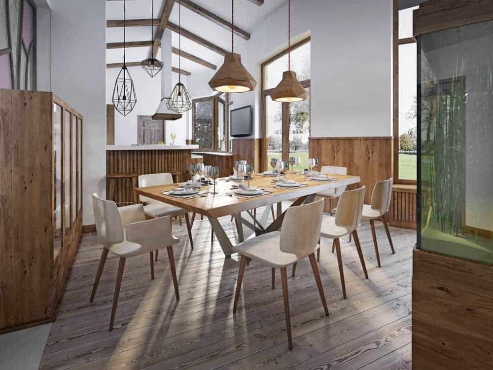 的餐厅提供木制吊坠灯照亮的餐桌和椅子。光木板地板,拱形天花板内衬暴露木梁上。