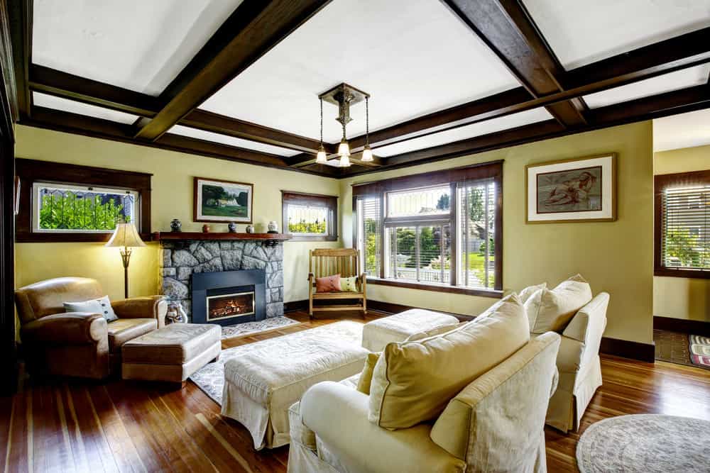 宽敞正式的工匠风格客厅设有带裸露横梁的天花板、硬木地板、小地毯和一座壁炉。