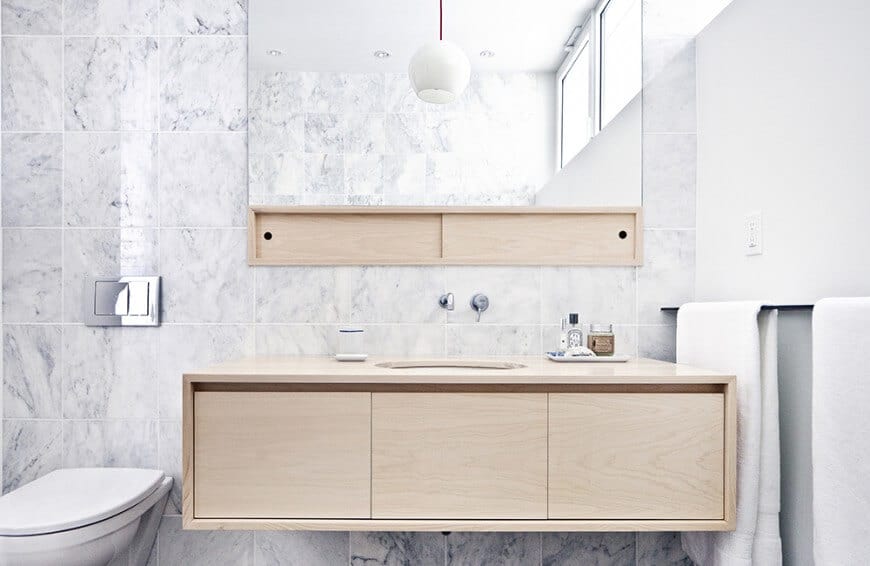 主浴室带有一个厕所，配有轻木浮动洗手台和一面镜子，固定在白色大理石瓷砖墙上。