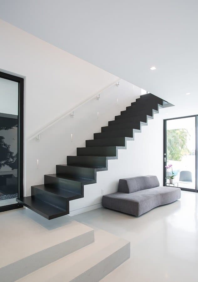 一个极简主义的入口，充满了灰色天鹅绒沙发和黑色楼梯，没有栏杆，由固定在白色墙壁上的楼梯灯照明。
