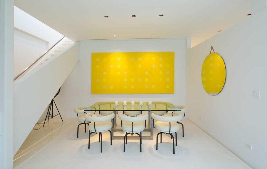 优雅的餐厅和一个时髦的玻璃餐桌设置与白色迷人的席位。黄色的墙壁装饰肯定是一个有吸引力的片墙设计。