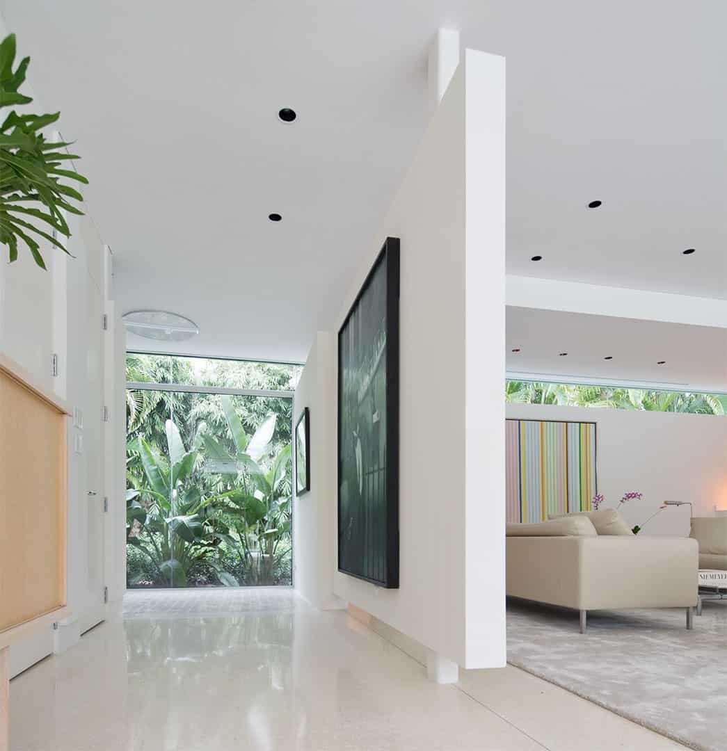 门厅设有白色的墙壁和地板以及巨大的墙壁装饰。玻璃墙和窗户可以俯瞰外面美丽的绿色植物。