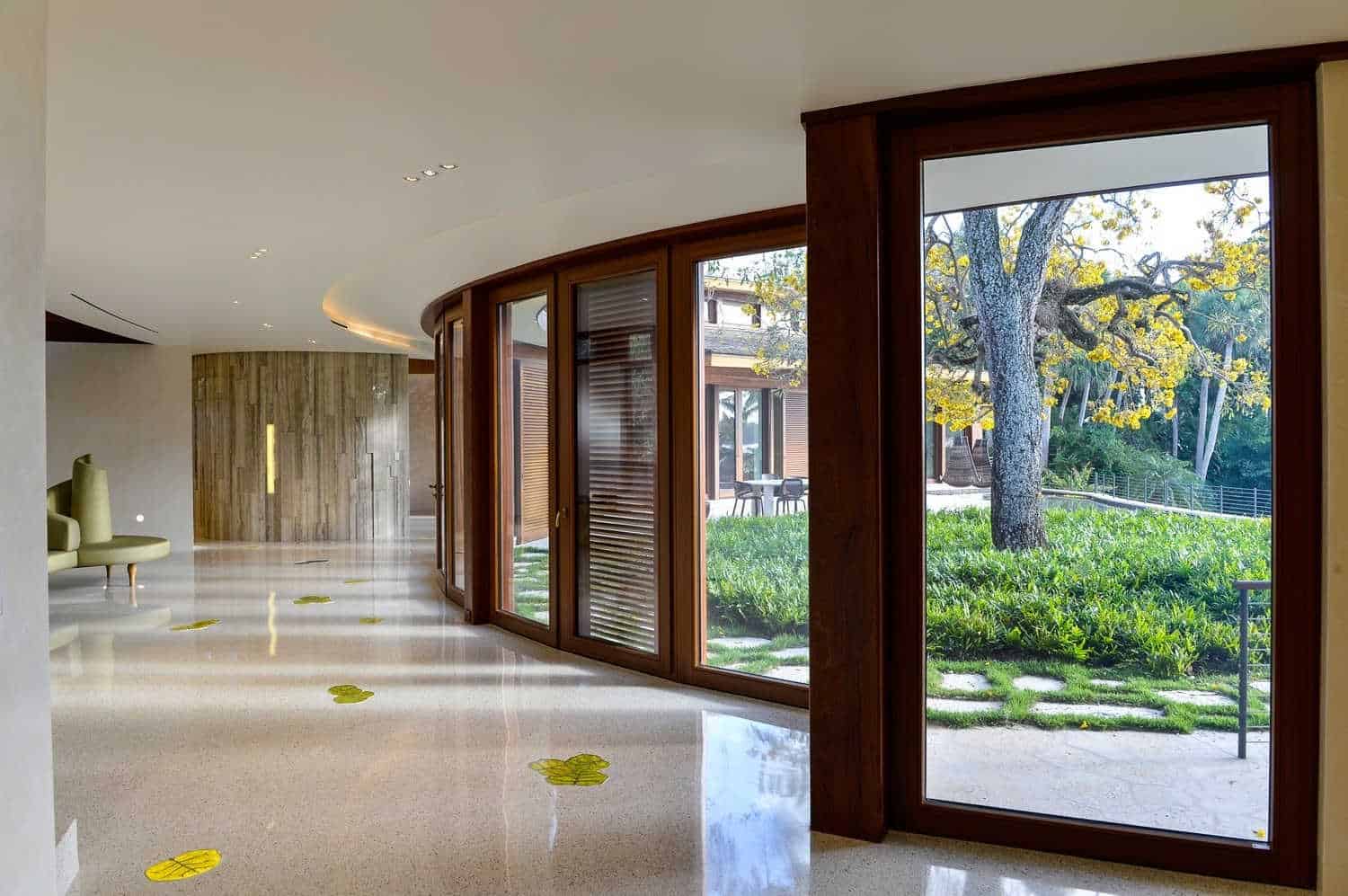 弯曲的门厅设有木质框架玻璃墙和优雅的大理石地板，强调与户外绿色植物艺术。
