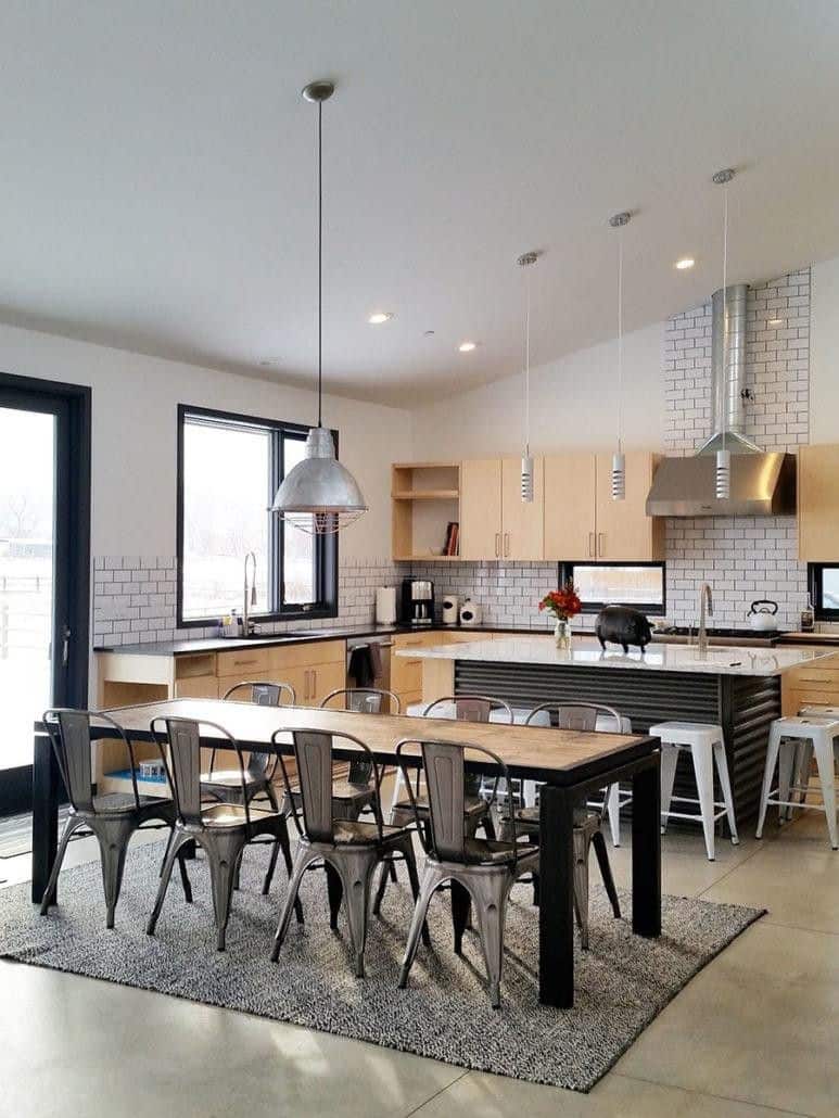 一间内吃式厨房，有一张矩形桌子和灰色椅子，与早餐岛平行。它铺着混凝土地板，上面铺着灰色的地毯。
