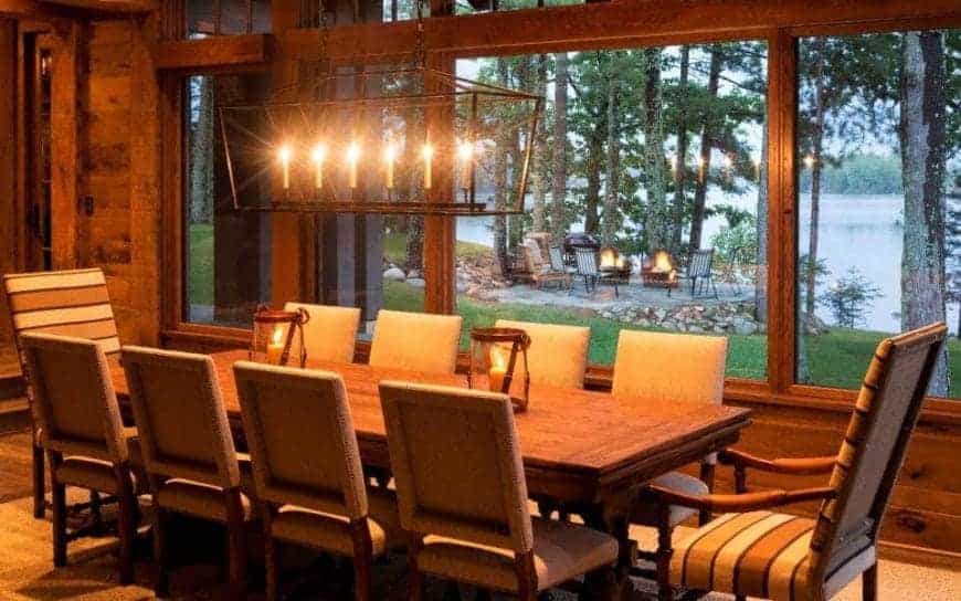 温暖的黄色灯光沐浴着整个乡村风格的餐厅，来自于悬挂在木制餐桌和软垫椅子上的锻铁排吊灯。这些都与宽阔的玻璃窗所呈现的可爱的湖畔景色相得益彰。