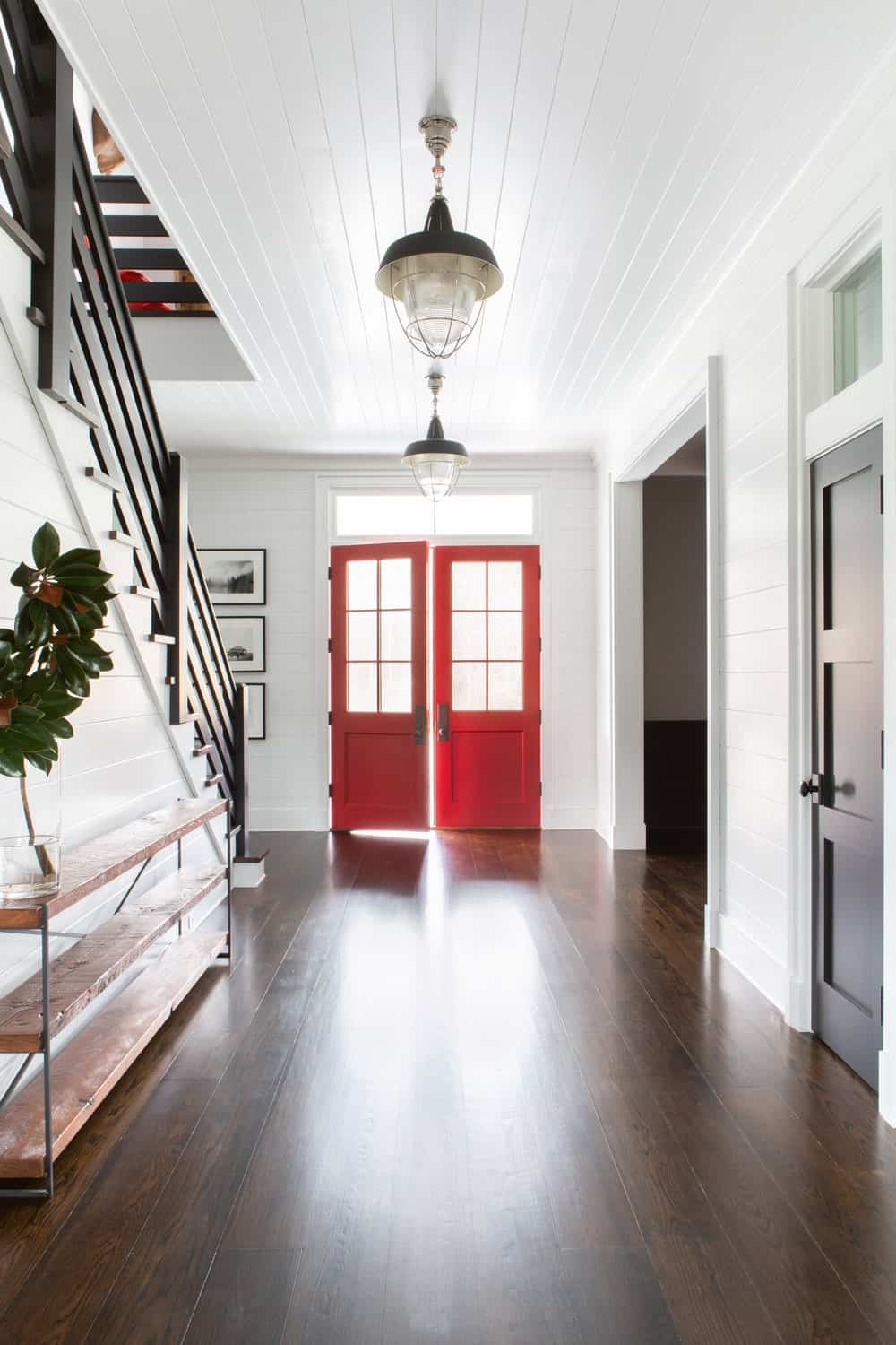 这是一个美丽而简单的欢迎门厅，有一对红色的木制正门，上面有玻璃板，为深色的硬木地板和白色的吊坠天花板带来了充足的自然光线。