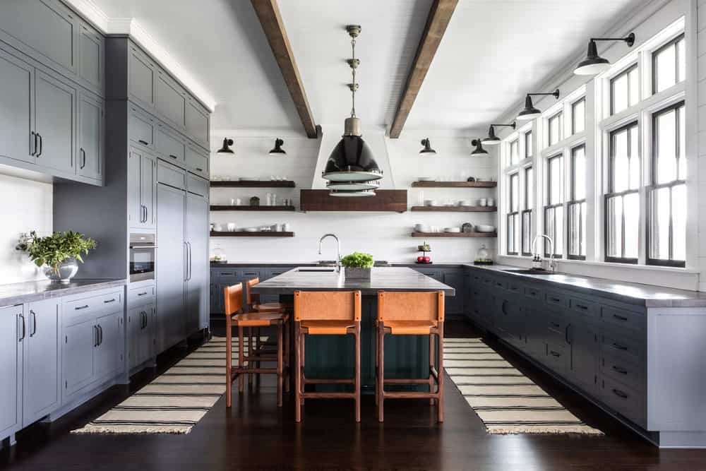 这间明亮宽敞的厨房在白色天花板上有几根裸露的木梁，与大l形半岛上的灰色摇床柜和抽屉相辅相成，厨房岛台位于深色硬木地板中间。