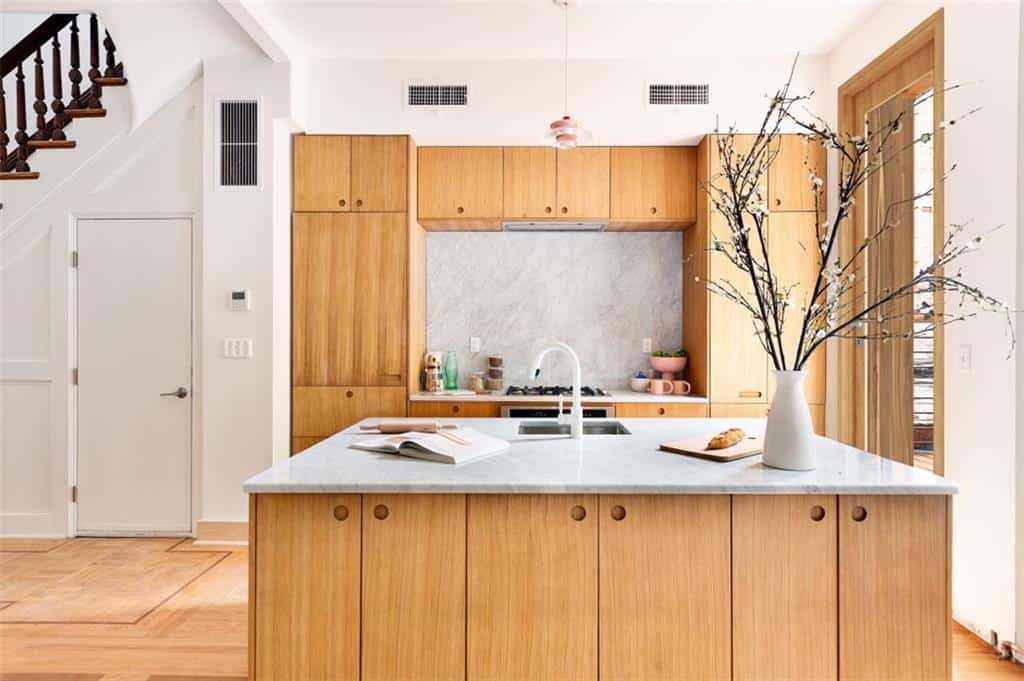 这个斯堪的纳维亚风格厨房的厨房岛有木制的内置橱柜，与一面墙上的巨大结构相匹配。这些木质元素与硬木地板融为一体，并与白色天花板形成对比。