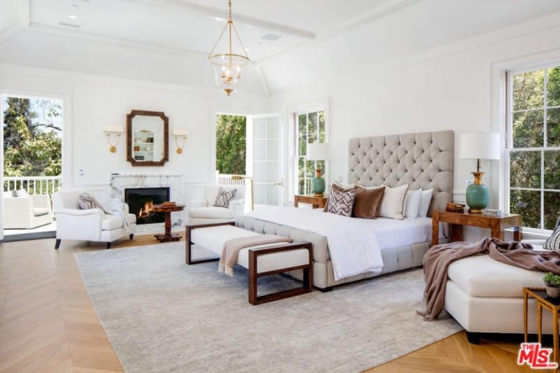 宽敞的白色主卧室，配有豪华的床和优雅的地毯，覆盖着人字形硬木地板。