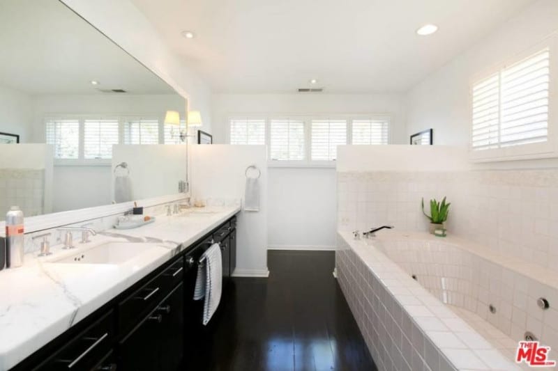 这个大型双梳妆台主浴室由深色抛光木地板和配套的橱柜内衬整个墙壁带来了生活。整个墙壁和白色瓷砖排列在淋浴间和嵌入式浴缸中，使木质组件非常流行。