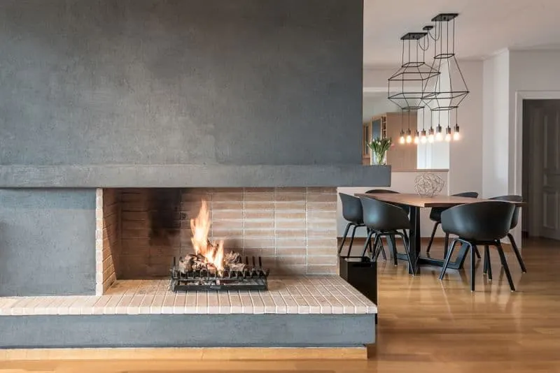开放的砖壁炉木炭墙上固定在这个餐厅特色工业侧灯,挂在一个木制的餐桌和黑色圆背椅子。