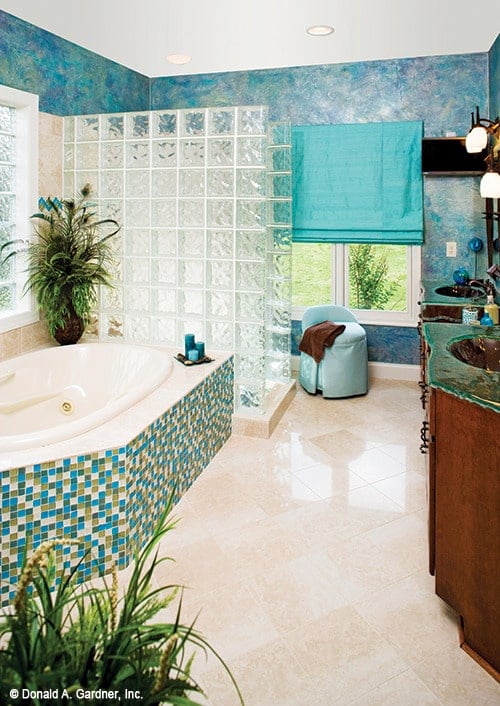 主浴室有醒目的蓝色墙壁，带有破旧柜台的双层梳妆台，一个覆盖着蓝色马赛克瓷砖的浴缸，以及一个用玻璃砌块板围起来的步入式淋浴间。
