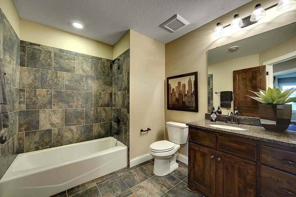 卫生间旁边的淋浴区墙上贴着灰色大理石瓷砖，与地板相呼应，与深色木质梳妆台相得益彰，梳妆台顶部有一盏壁挂灯。