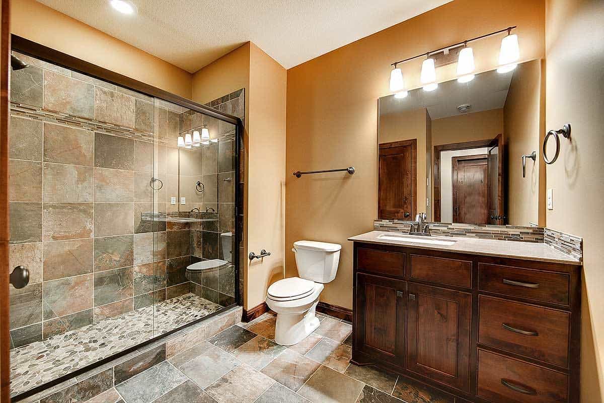 另一间浴室里有一个黑色木制的小梳妆台、卫生间和一个玻璃围成的步入式淋浴区，淋浴区有各种灰色大理石状瓷砖，与浴室的地板相配。