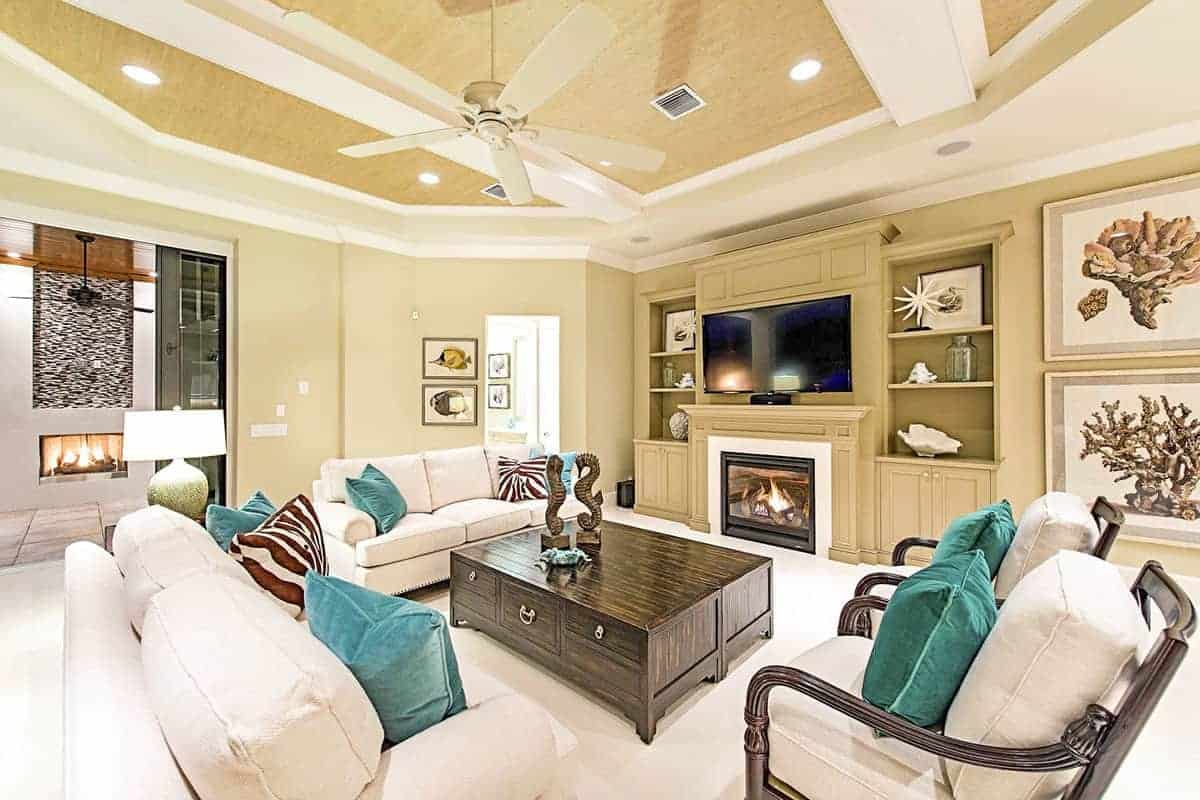 沙发和扶手椅的白色靠垫与地毯地板相融合，使深色木制咖啡桌脱颖而出。米黄色的墙壁与大型木结构融合在一起，壁炉和电视两侧的架子。