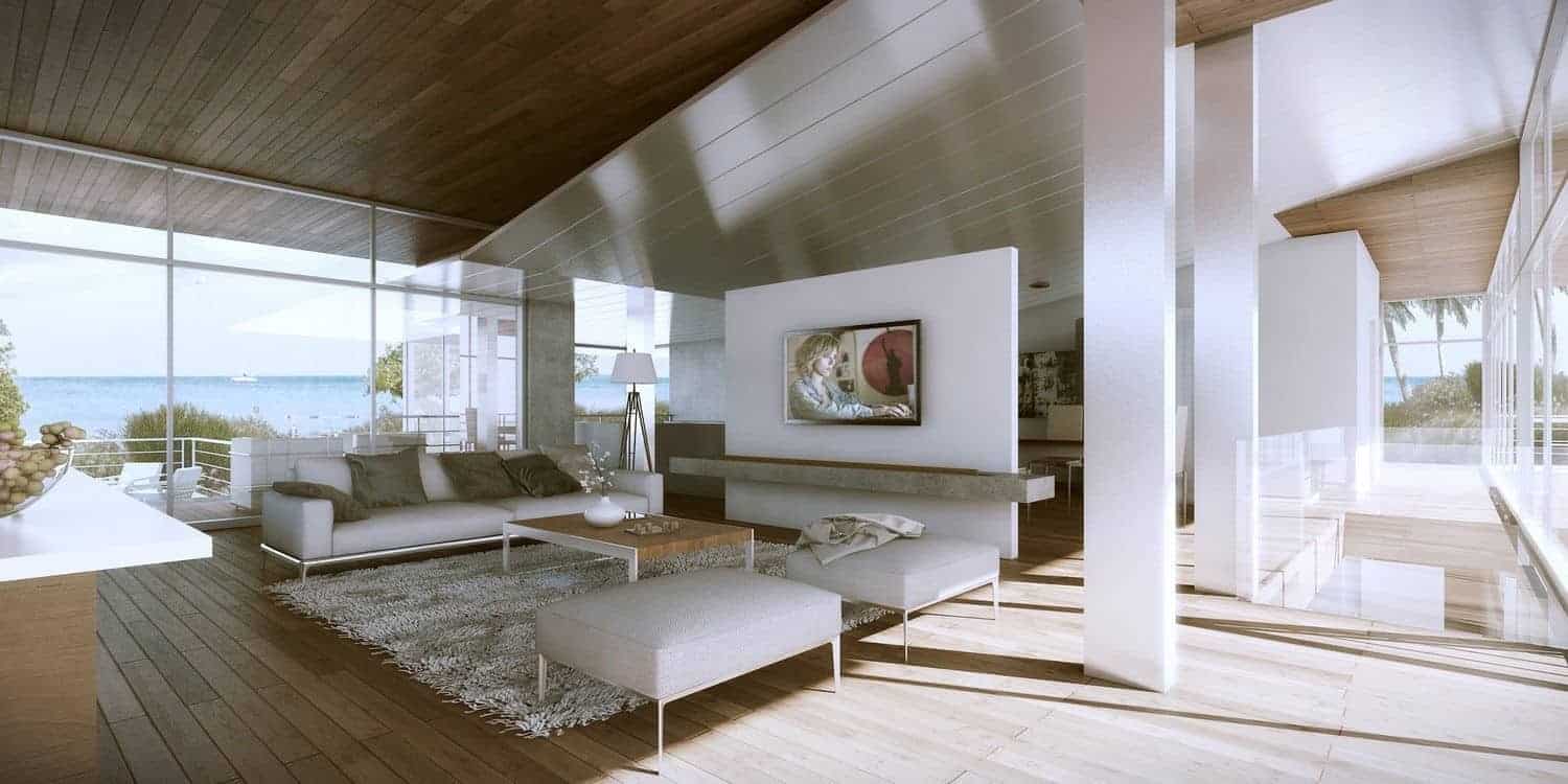 这个宽敞的客厅被玻璃墙进一步提亮，玻璃墙以美丽的海滨景色为特色，为硬木地板带来了充足的自然光，与白色现代沙发组和白色支撑柱形成对比。