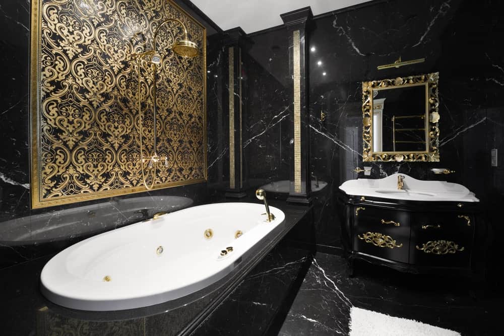 这个浴室迷人的黑色大理石墙壁和地板与梳妆台、镜子和浴缸上方的墙壁艺术等复杂的金色细节相结合。
