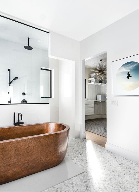 独立的铜浴缸与原始的白墙和主浴室的花纹瓷砖地板形成鲜明对比。