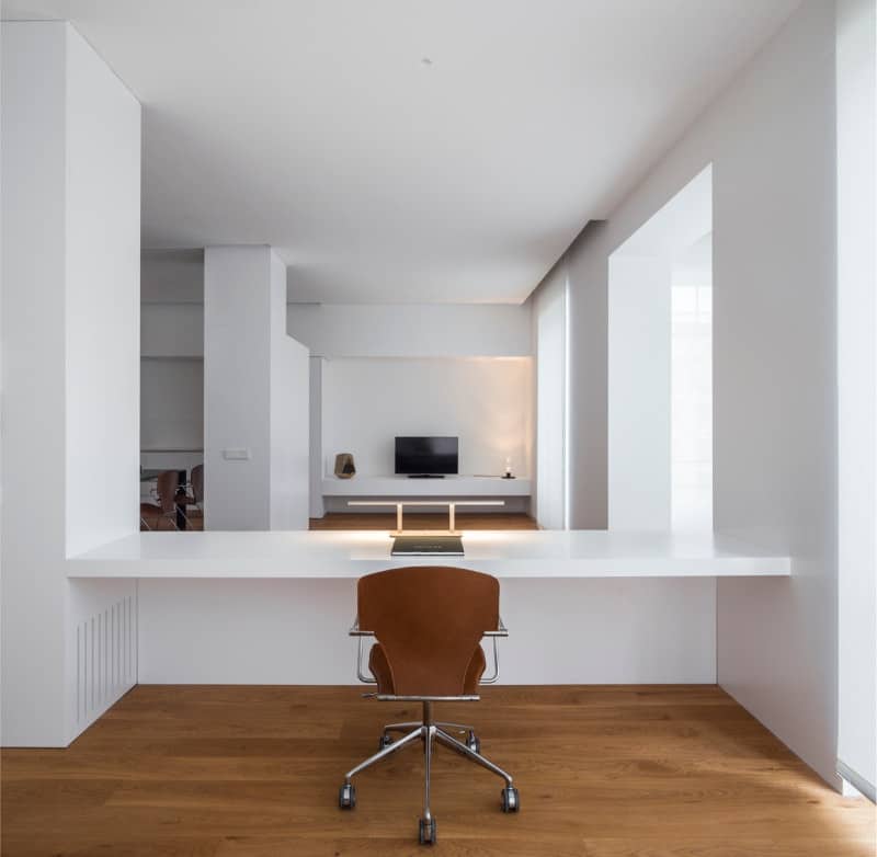 在这间极简主义风格的家庭办公室里，一把棕色的办公椅放在一张内置的白色办公桌前。