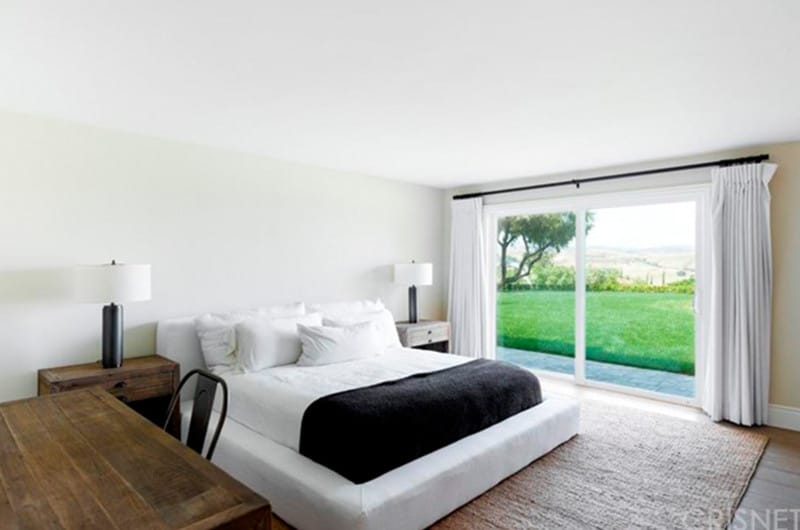 一个极简主义的客房简化了铺着地毯的床空间，大窗户可以俯瞰院子里的美景，两盏侧灯和一张学习桌。