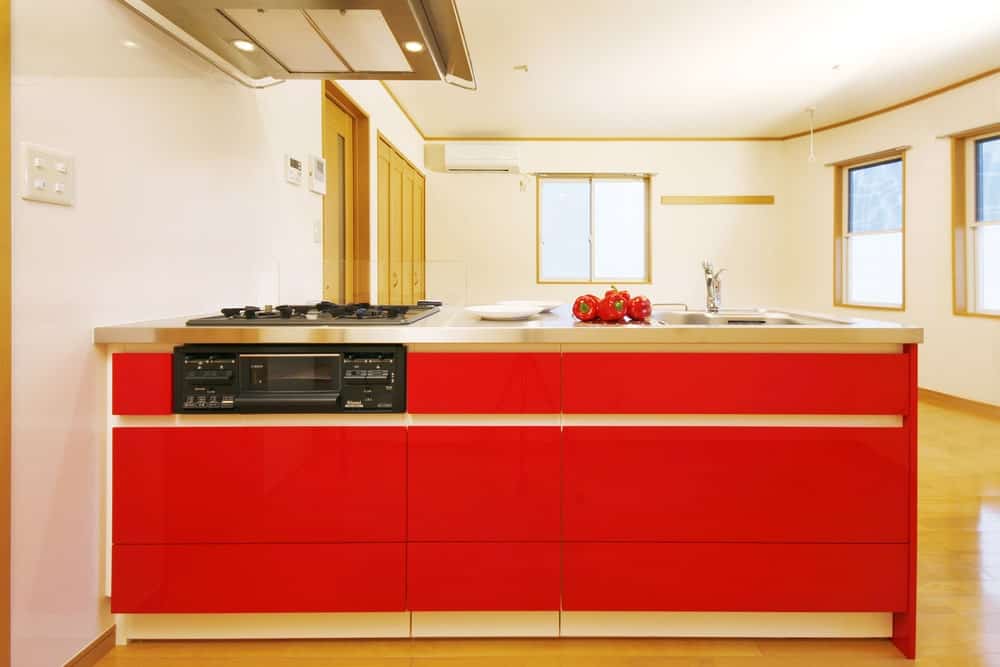 白色厨房拥有一个带有不锈钢台面和水槽的红色半岛。它还有一个内置灶台，通风罩安装在白色天花板上。