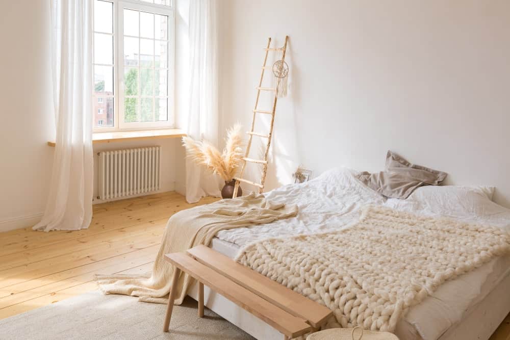 主卧室的大床铺在硬木地板上。侧面的玻璃窗有可爱的白色窗帘。