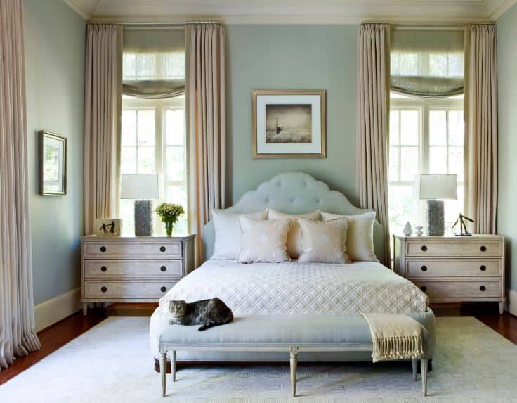 这是一间简单而别致的主卧室，在传统床的浅绿色床头板两侧有一对破旧的床头抽屉，床脚有一张低矮的软垫长椅，与绿色的墙壁相匹配。