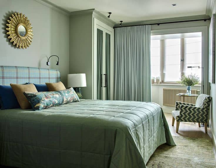 明亮的窗户搭配着浅绿色的窗帘，与绿色的墙壁融为一体，在软垫床头板上方有金色的壁挂式太阳般的艺术品。