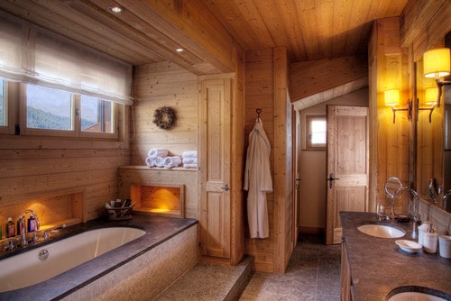 这是一间类似桑拿浴的主浴室，有木墙和天花板。凹形浴缸周围环绕着木材和情调照明。