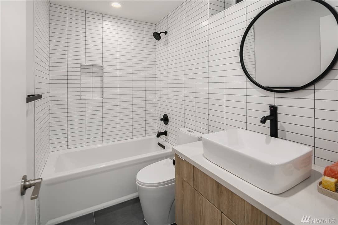 这个斯堪的纳维亚风格的浴室有白色瓷砖的墙壁，配以黑色的灌浆，以强调瓷砖的直线。这一主题由房间的黑色固定装置和圆形壁挂镜的框架补充。