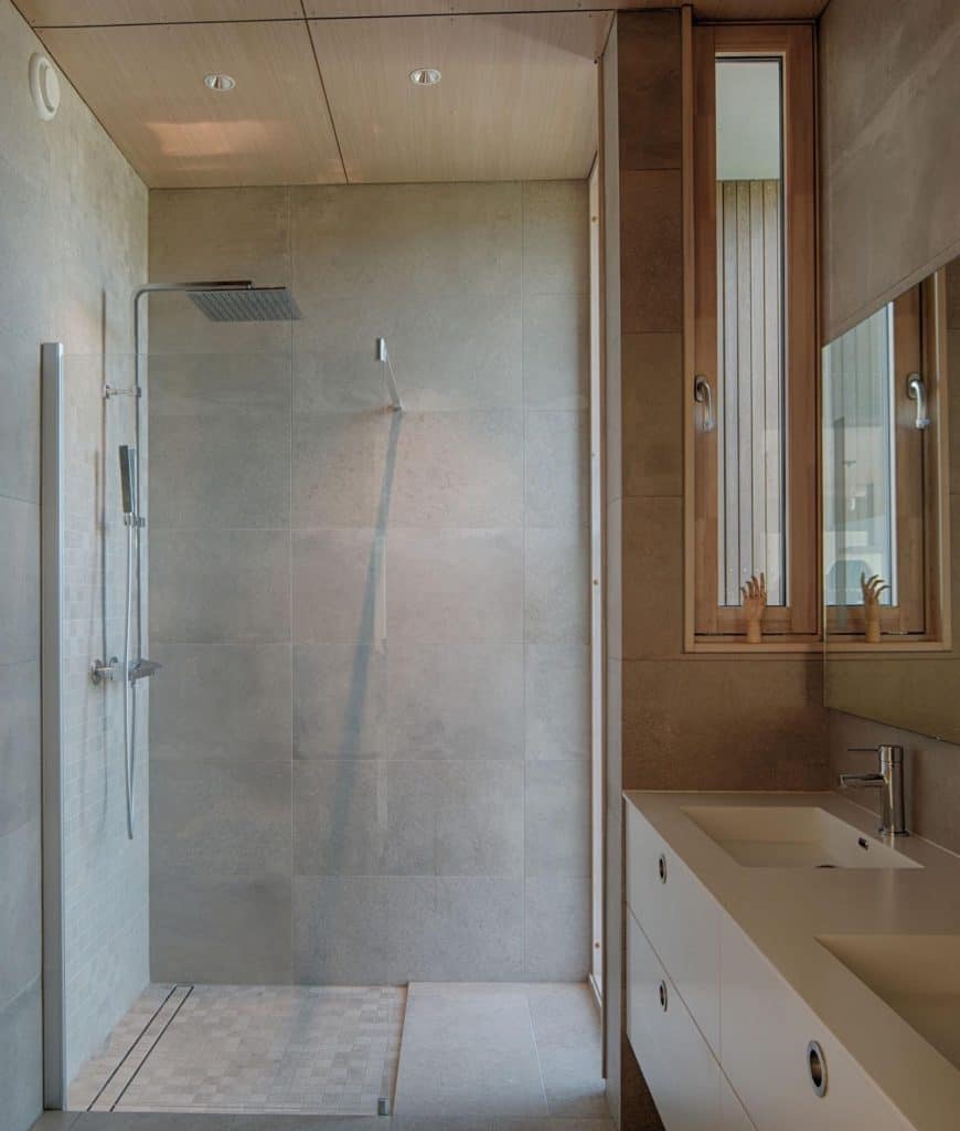 淋浴区与斯堪的纳维亚风格浴室的其余部分被玻璃门隔开，玻璃门与灰色墙壁无缝融合。它有现代化的淋浴装置，与梳妆台区域的水龙头相匹配，梳妆台有一个白色的台面。