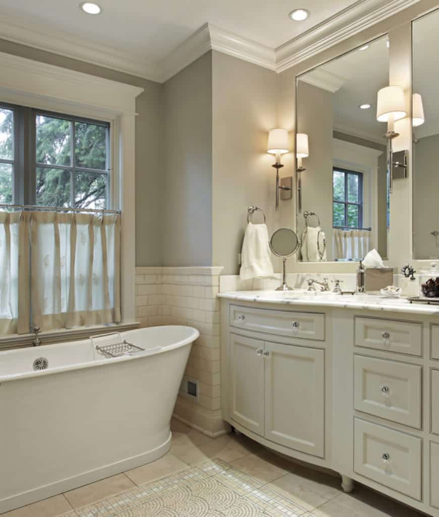 独立的白色浴缸被放置在落地窗旁边的角落里。梳妆台区建在灰色的墙壁里，里面有白色的木制橱柜和抽屉，抽屉的水晶把手被白色天花板上的针线灯照亮。