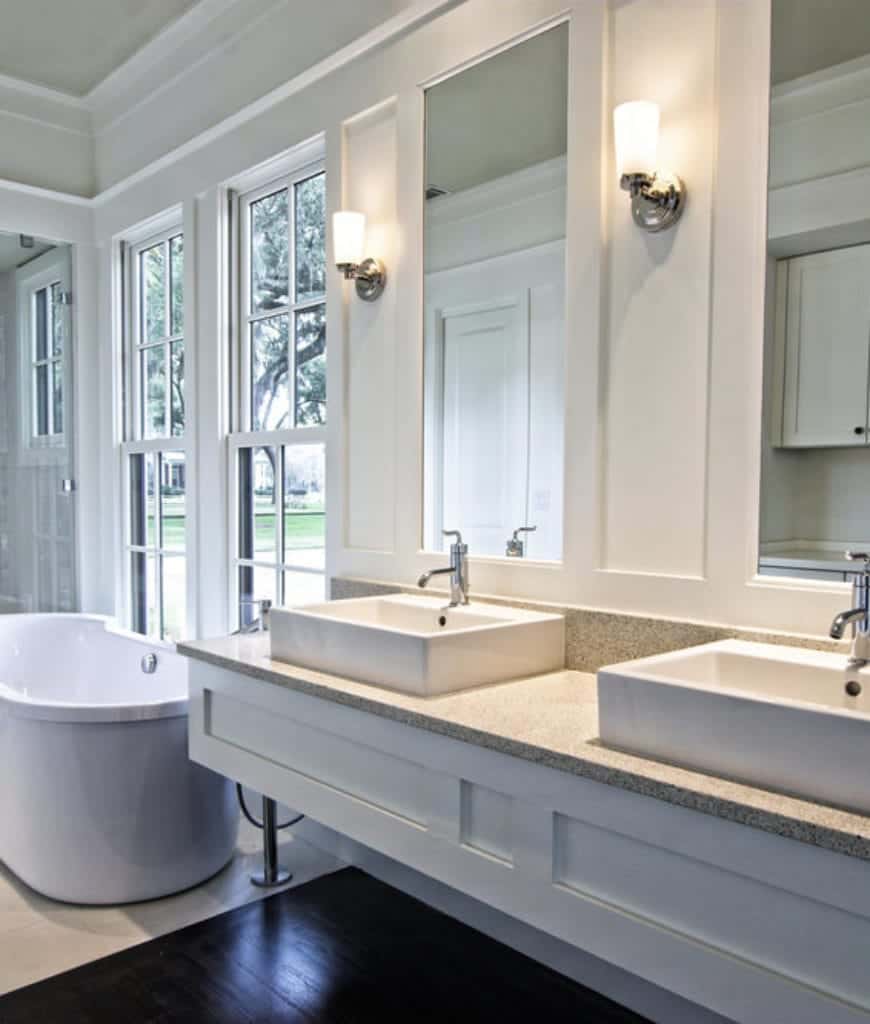 高大的梳妆镜嵌在白色木质墙面中，两侧装有现代壁挂灯，与水龙头相呼应。梳妆台的水槽与落地窗边的独立浴缸相匹配。