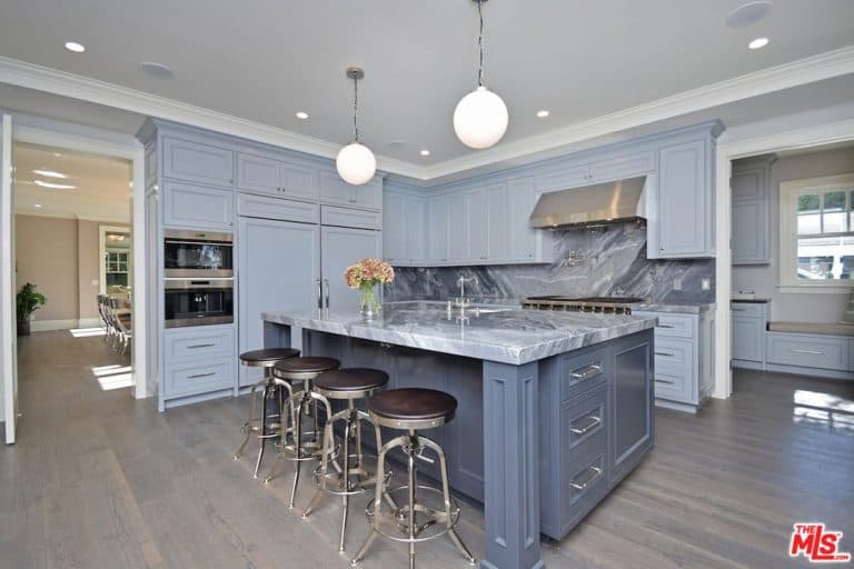这间厨房配备了灰色的橱柜、厨房柜台和中央岛台，配有令人惊叹的台面，类似于厨房的后挡板。