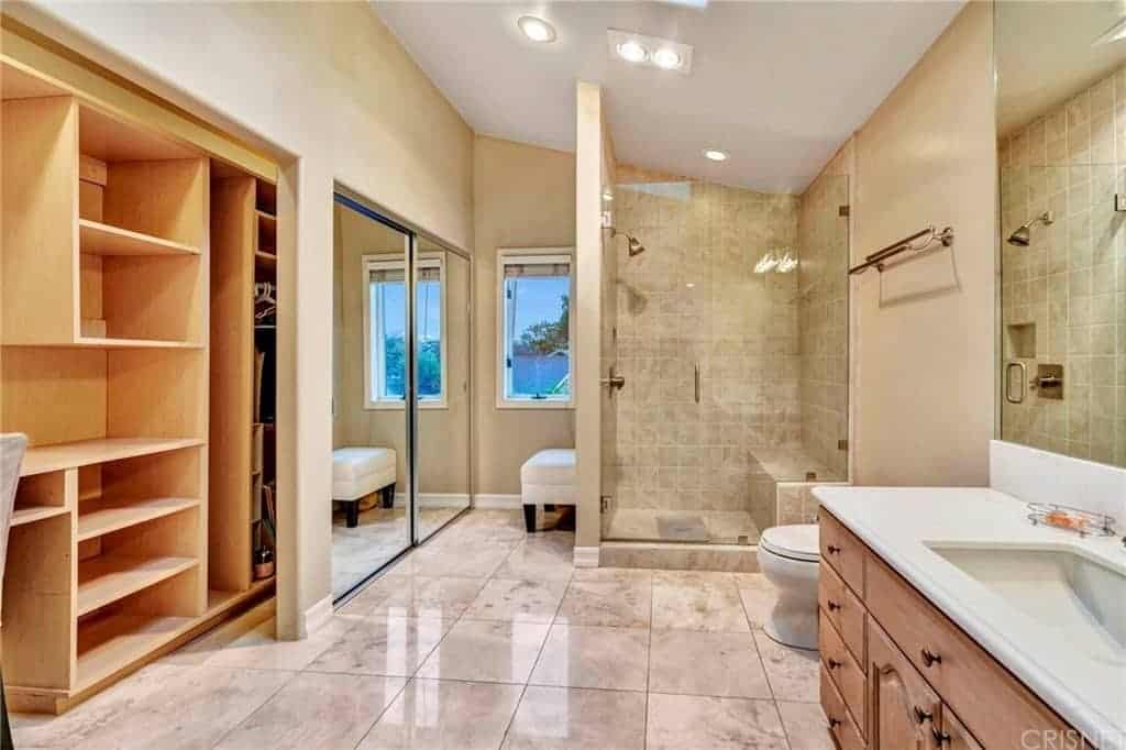 这间主浴室的白色棚顶与米黄色墙壁和白色大理石瓷砖地板搭配，使木制梳妆台和玻璃围合的淋浴区脱颖而出。