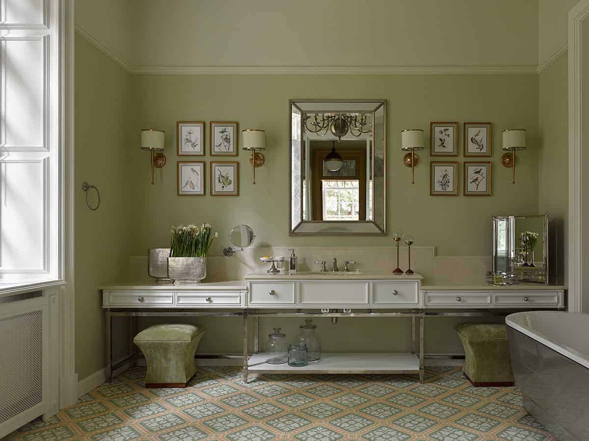 可爱的绿色和粉色图案的地砖与主卧室相得益彰。主卧室的绿色墙壁上装饰着装裱好的艺术品、壁灯和一面梳妆镜，镜子位于有抽屉的水槽上方的中间。