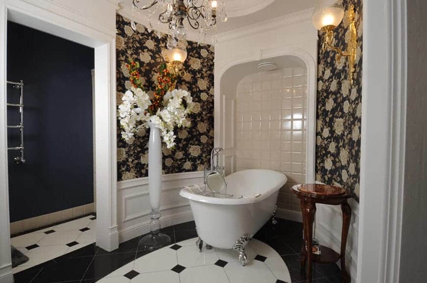 这是一间别致的浴室，墙壁上装饰着碎花墙纸，白色装饰和护墙板与瓷砖地板的黑色细节形成对比。